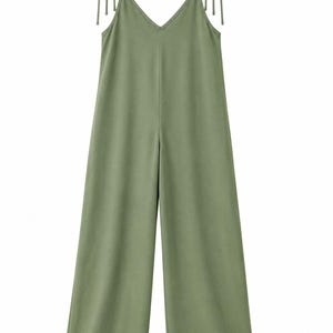 May include: A solid sage green jumpsuit featuring a V-neckline and wide-leg trousers. The garment includes thin shoulder straps that tie into bows at the top, providing an adjustable fit. The design is simple, sleeveless, and has a straight silhouette.