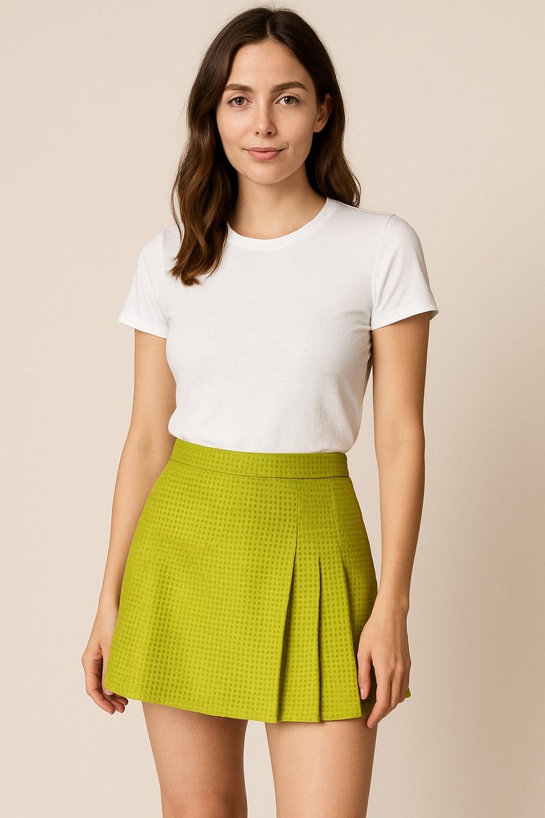 May include: A woman wearing a white t-shirt and a green pleated skirt. The skirt has a checkered pattern.