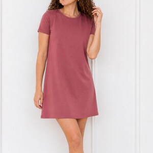 May include: A solid mauve-colored short-sleeve mini dress featuring a simple crew neckline and a straight, relaxed silhouette that falls above the knee. The garment is constructed from a smooth, plain fabric with no visible patterns, prints, or textures.