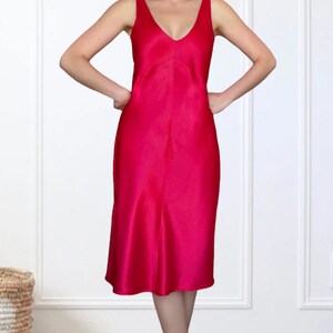 K&ouml;nnte beinhalten: Ein leuchtend pinkfarbenes, &auml;rmelloses Midikleid aus seidenweichem Satin. Das Kleid hat einen V-Ausschnitt und eine flie&szlig;ende Silhouette.