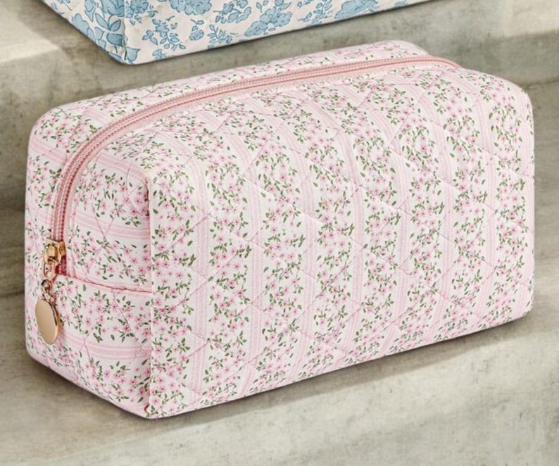 May include: A pink quilted makeup bag with a floral pattern. The bag has a zipper closure and a gold zipper pull.