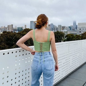 May include: A green linen crop top with a lace-up back detail. The top is worn with light blue denim jeans.