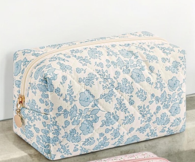 May include: A white quilted makeup bag with a blue floral pattern. The bag has a zipper closure and a gold zipper pull.