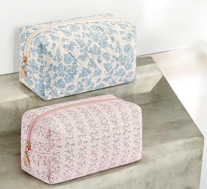 May include: Two quilted fabric cosmetic bags. The top bag is light blue with a white background and a floral pattern. The bottom bag is pink with a white background and a floral pattern.