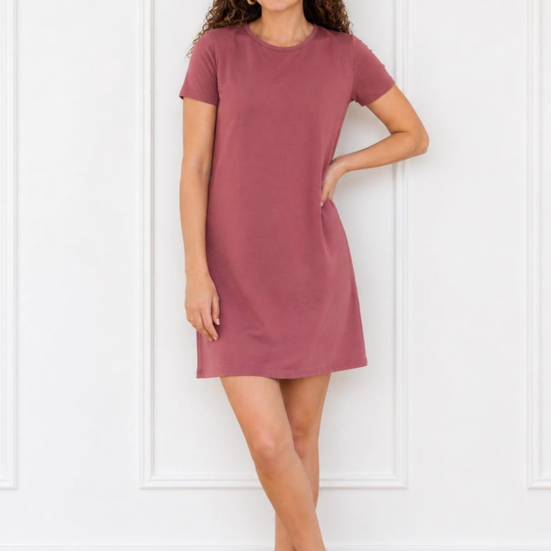 May include: A solid mauve-colored short-sleeve mini dress featuring a simple crew neckline and a straight, relaxed silhouette that falls above the knee. The garment is constructed with a plain, smooth fabric finish and has a clean, unadorned design.