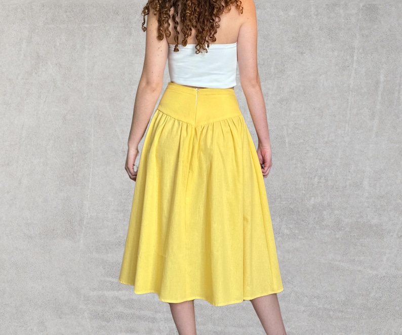 May include: A bright yellow midi skirt with a high waist and a flared silhouette. The skirt is made of a lightweight fabric and has a gathered detail at the waist. The skirt is paired with a white tube top.