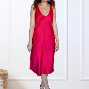 K&ouml;nnte beinhalten: Eine Frau tr&auml;gt ein hellrosa, &auml;rmelloses Satin-Midikleid.