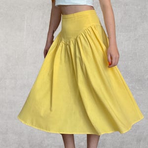 May include: A bright yellow skirt with a high waist and a flared A-line silhouette. The skirt features a gathered detail at the waistline, creating a full, flowing look. The fabric appears to be a lightweight material, suitable for warmer weather.