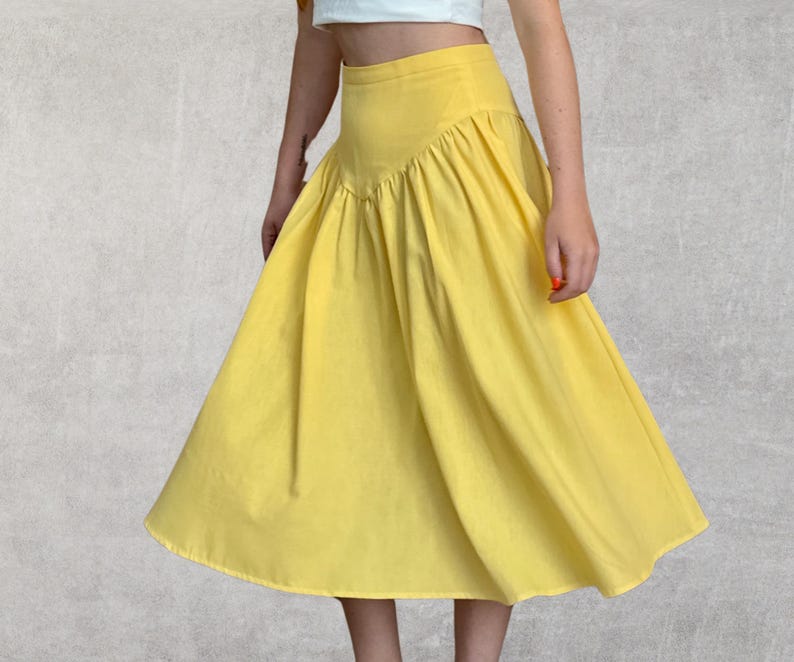 May include: A bright yellow skirt with a high waist and a flared A-line silhouette. The skirt features a gathered detail at the waistline, creating a full, flowing look. The fabric appears to be a lightweight material, suitable for warmer weather.