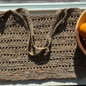 May include: A large, crocheted tote bag made of natural fibers with green accents. The bag has a wide, open top and two long straps.