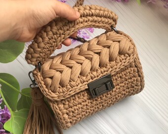 May include: A small, brown crocheted handbag with a chain strap and a tassel. The bag has a flap closure with a metal clasp.