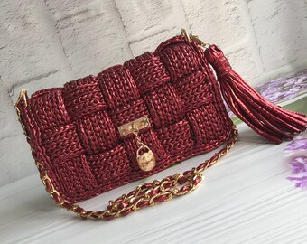 May include: A red woven handbag with a gold chain strap and a gold lock charm. The bag has a tassel detail.