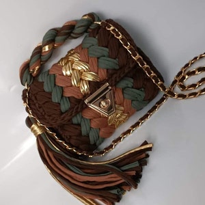 May include: A small, brown, green, and gold woven handbag with a gold chain strap and tassel. The bag has a gold clasp.