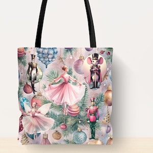 May include: A pink and blue tote bag with a Christmas Nutcracker theme. The bag features a repeating pattern of ballerinas, nutcrackers, and Christmas ornaments. The bag has black handles.