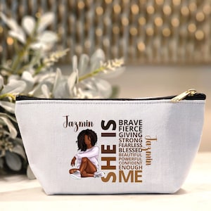 May include: White canvas makeup bag with a zipper closure. The bag features a brown illustration of a woman with curly hair and the text "Jazmin SHE IS BRAVE FIERCE GIVING STRONG FEARLESS BLESSED BEAUTIFUL POWERFUL CONFIDENT ENOUGH ME Jazmin".