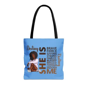 Pu&ograve; includere: Una borsa tote blu chiaro con un manico nero. La borsa presenta una grafica di una donna con la pelle marrone e i capelli neri. Il testo "Destiny SHE IS" &egrave; in lettere marroni e nere. Il testo "BRAVE FIERCE GIVING STRONG FEARLESS BLESSED BEAUTIFUL POWERFUL CONFIDENT ENOUGH ME" &egrave; in lettere marroni. Il testo "Destiny" &egrave; in lettere nere.