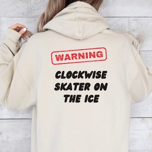 May include: Beige hoodie with a red warning sign that says "WARNING" and black text that says "CLOCKWISE SKATER ON THE ICE"
