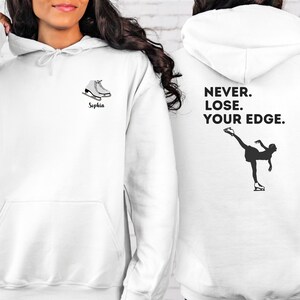May include: White hoodie with a black silhouette of a figure ice skating on the back. The text "NEVER. LOSE. YOUR EDGE." is printed above the figure. The front of the hoodie has a pair of white ice skates and the name "Sophia" printed below.