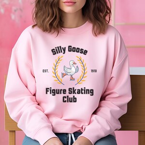 May include: Pink sweatshirt with a black graphic of a goose figure skating. The graphic says "Silly Goose Figure Skating Club" with "EST. 1910" underneath.