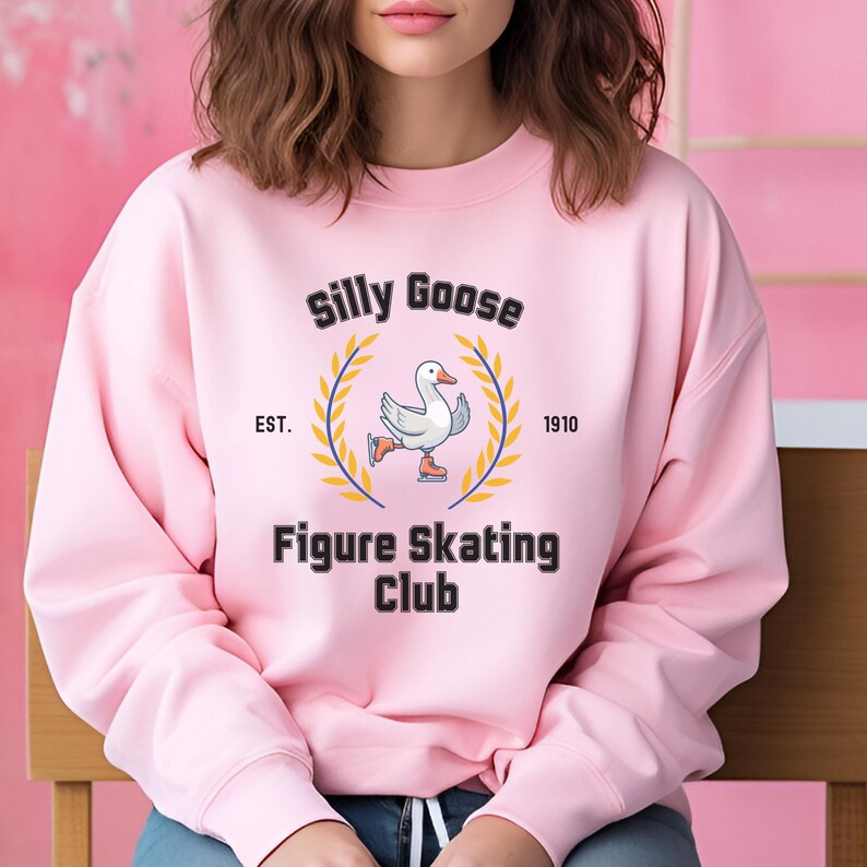 May include: Pink sweatshirt with a black graphic of a goose figure skating. The graphic says "Silly Goose Figure Skating Club" with "EST. 1910" underneath.