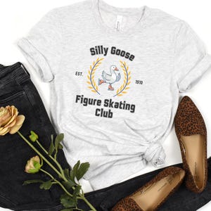 May include: A gray t-shirt with a white graphic of a goose figure skating. The graphic says "Silly Goose Figure Skating Club" with "Est. 1910".