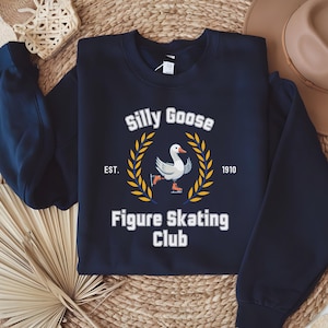 May include: A navy blue sweatshirt with a white goose wearing ice skates and the text "Silly Goose Figure Skating Club" with the dates "EST. 1910" on a white background.