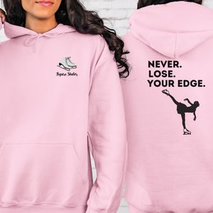May include: Pink hoodie with a figure skater graphic on the front and the text "NEVER. LOSE. YOUR EDGE." on the back.