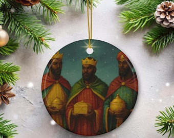 May include: A round Christmas ornament featuring an illustration of the three wise men. Each figure wears a crown and holds a gift. The background is a starry night scene. The ornament is trimmed with a gold cord.