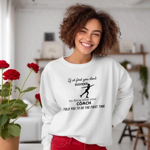 May include: White sweatshirt with the text "If at first you don't succeed, try doing what your coach told you to do the first time." The graphic shows a figure skater. The sweatshirt is a crew neck style.