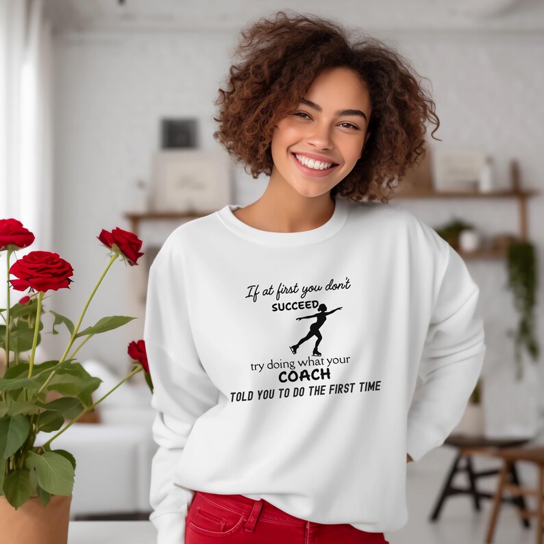 May include: White sweatshirt with the text "If at first you don't succeed, try doing what your coach told you to do the first time." The graphic shows a figure skater. The sweatshirt is a crew neck style.