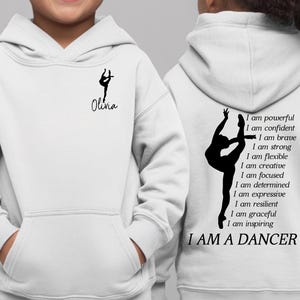 May include: White hoodie with a front pocket and a hood. The front features a black silhouette of a dancer and the name "Olivia". The back displays a dancer silhouette and the text "I AM A DANCER" with inspirational affirmations.