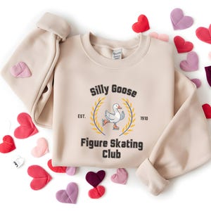 May include: A beige sweatshirt with a graphic of a goose ice skating and the text "Silly Goose Figure Skating Club Est. 1910".