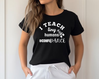 May include: Black t-shirt with white text that reads "I teach tiny humans #CONFIDENCE" and a pair of white ballet shoes.