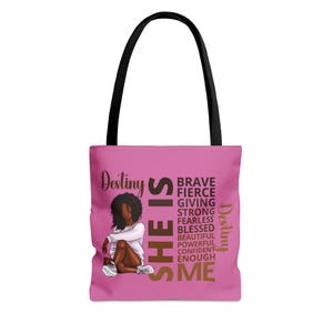 Pu&ograve; includere: Borsa tote rosa con manico nero e un'immagine di una donna con i capelli castani e una camicia bianca. Il testo sulla borsa recita "Destiny SHE IS BRAVE FIERCE GIVING STRONG FEARLESS BLESSED BEAUTIFUL POWERFUL CONFIDENT ENOUGH ME Destiny".