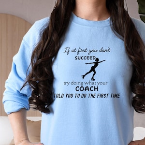 May include: Light blue sweatshirt with black text and a figure skater graphic. The text reads "If at first you don't succeed, try doing what your coach told you to do the first time."