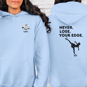 May include: Light blue hoodie with a pair of white ice skates and the name "Sophia" on the front. The back of the hoodie has a silhouette of a figure skater and the text "NEVER. LOSE. YOUR EDGE."