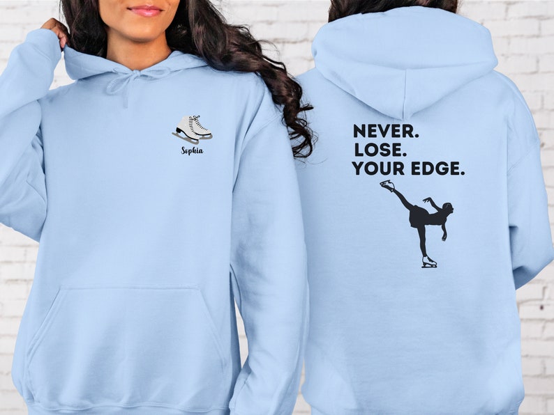 May include: Light blue hoodie with a pair of white ice skates and the name "Sophia" on the front. The back of the hoodie has a silhouette of a figure skater and the text "NEVER. LOSE. YOUR EDGE."
