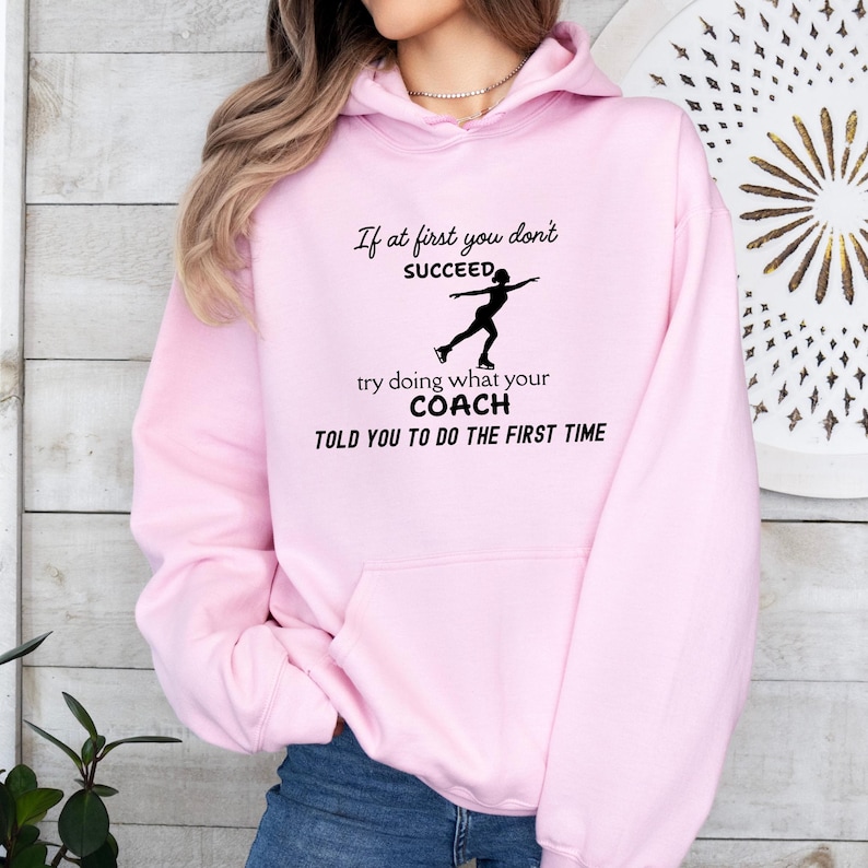May include: A light pink hoodie with a black graphic of a figure skater and text that reads "If at first you don't SUCCEED, try doing what your COACH TOLD YOU TO DO THE FIRST TIME."