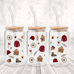 Peut inclure: Trois verres à boire en verre transparent avec des couvercles en bambou et des pailles. Chaque verre à boire présente un motif différent de carreaux rouges et noirs, de cabanes, de verres à vin et de sapins.