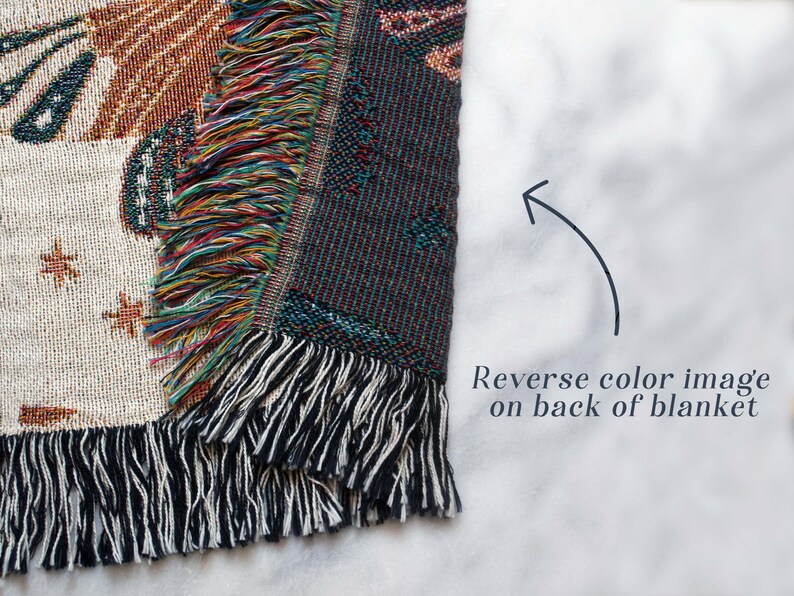 May include: A woven tapestry throw blanket with a colorful fringe. The front of the blanket features a white background with a design in brown, orange, and yellow. The back of the blanket features a reverse color image with a dark blue background.