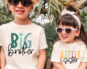 May include: Two children wearing matching white t-shirts with colorful text. The older child is wearing a straw hat and sunglasses and their shirt says "BIG brother". The younger child is wearing a pink headband and sunglasses and their shirt says "LITTLE sister".