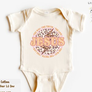 May include: A white baby onesie with a pink and brown leopard print circle design. The circle has the words "THE WAY THE TRUTH THE LIFE" around the outside and "JESUS" in large letters inside the circle.