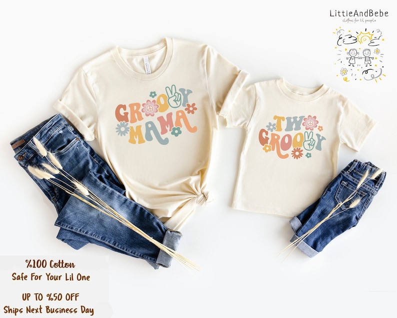 May include: Two matching t-shirts with a groovy theme. The larger shirt says "Groovy Mama" in colorful letters with peace signs and flowers. The smaller shirt says "Two Groovy" in colorful letters with peace signs and flowers.