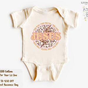 Puede incluir: Un body de beb&eacute; beige con un dise&ntilde;o circular de estampado de leopardo rosa y marr&oacute;n. El c&iacute;rculo tiene las palabras "THE WAY THE TRUTH THE LIFE" alrededor del exterior y "JESUS" en letras rosas grandes en el interior.