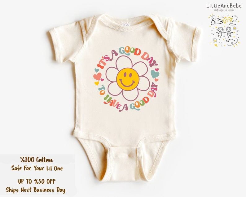 May include: A white baby onesie with a colorful graphic of a daisy with a smiley face. The text around the daisy reads "It's a good day to have a good day".