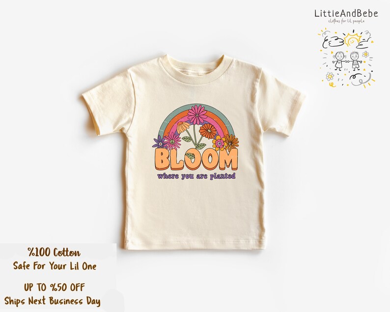 May include: A cream colored t-shirt with a rainbow and flowers graphic. The text "BLOOM where you are planted" is printed on the shirt.