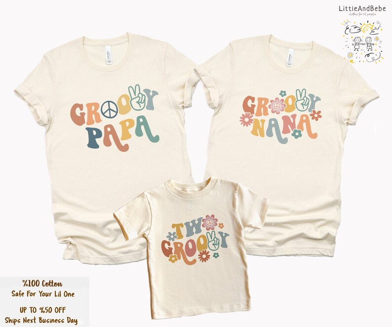 May include: Three cream-colored t-shirts with a retro groovy font design. The shirts say "Groovy Papa", "Groovy Nana", and "Two Groovy". Each shirt has a peace sign and flowers.