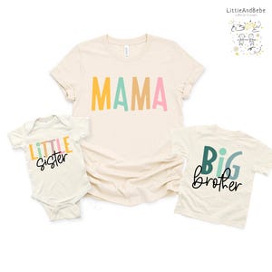 May include: Three cream-colored shirts with colorful text. A t-shirt with "MAMA" in yellow, pink, and teal. A onesie with "Little Sister" in yellow, orange, and green. A t-shirt with "Big brother" in teal and black.