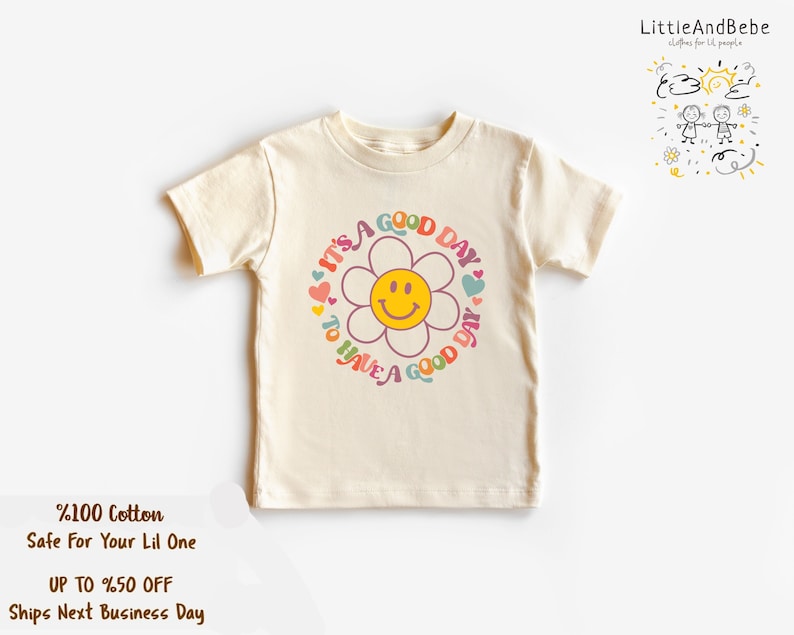 May include: A cream colored short-sleeved t-shirt with a colorful graphic of a flower with a smiley face and the text "It's a good day to have a good day".