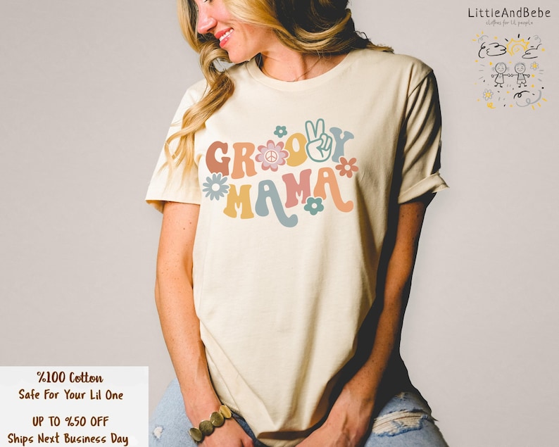 May include: A light beige t-shirt with the text "Groovy Mama" in colourful retro lettering with peace signs and flowers.